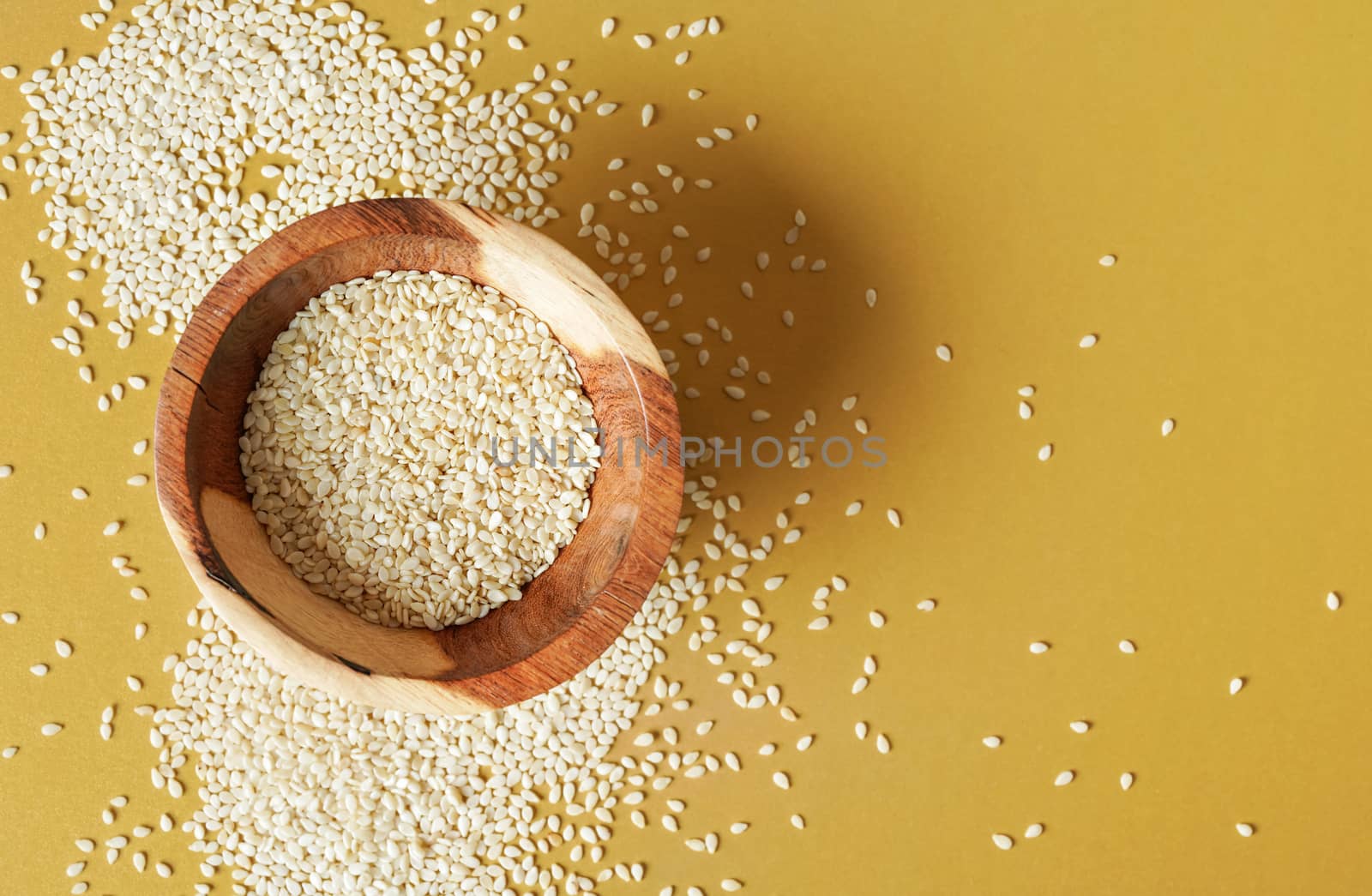 Tiny white sesame seeds in small wooden bowl, on yellow desk, view from above by Ivanko