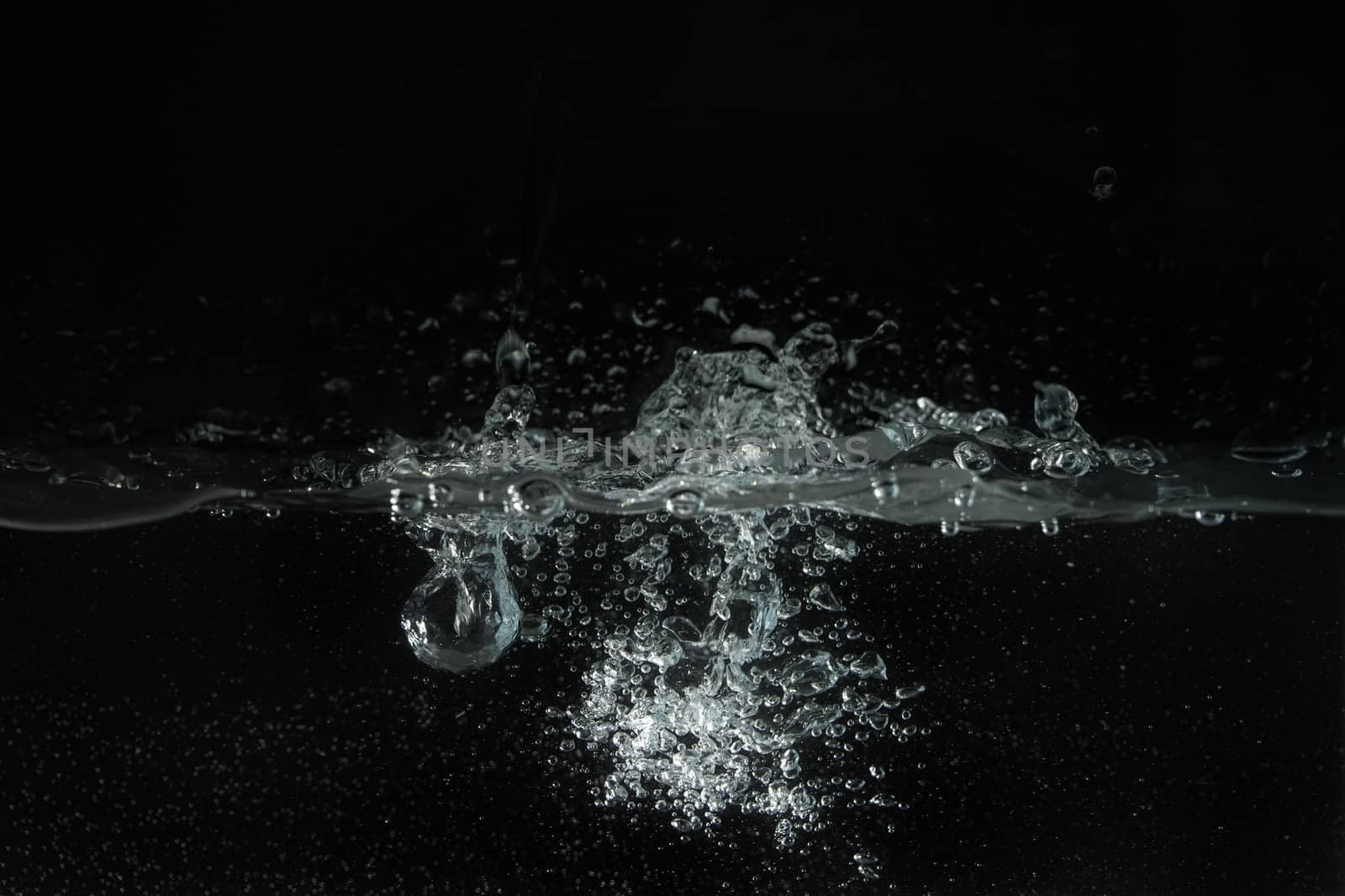 Water splashing as it's poured into aquarium tank, black background.