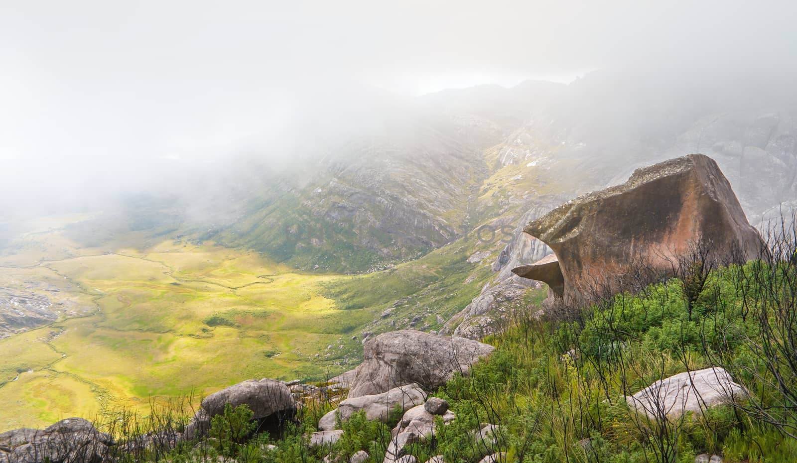 Typical landscape scenery seen during trek to pic Boby in Andringitra massif, Madagascar, sun lit valley down, some grass, bushes and large boulder in foreground by Ivanko