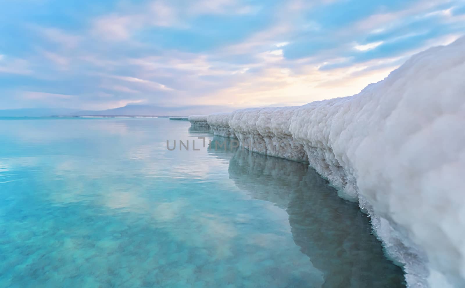 Sand completely covered with crystalline salt looks like ice or snow on shore of Dead Sea, turquoise blue water near, sky colored with morning sun distance - typical scenery at Ein Bokek beach, Israel by Ivanko