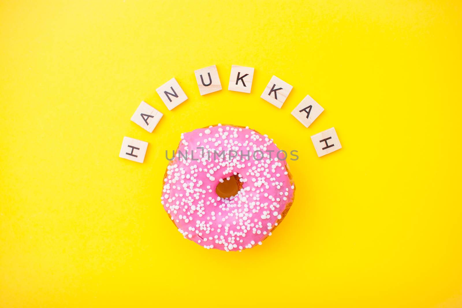 pink delicious donuts on yellow background and inscription from wooden blocks happy hanukkah by malyshkamju