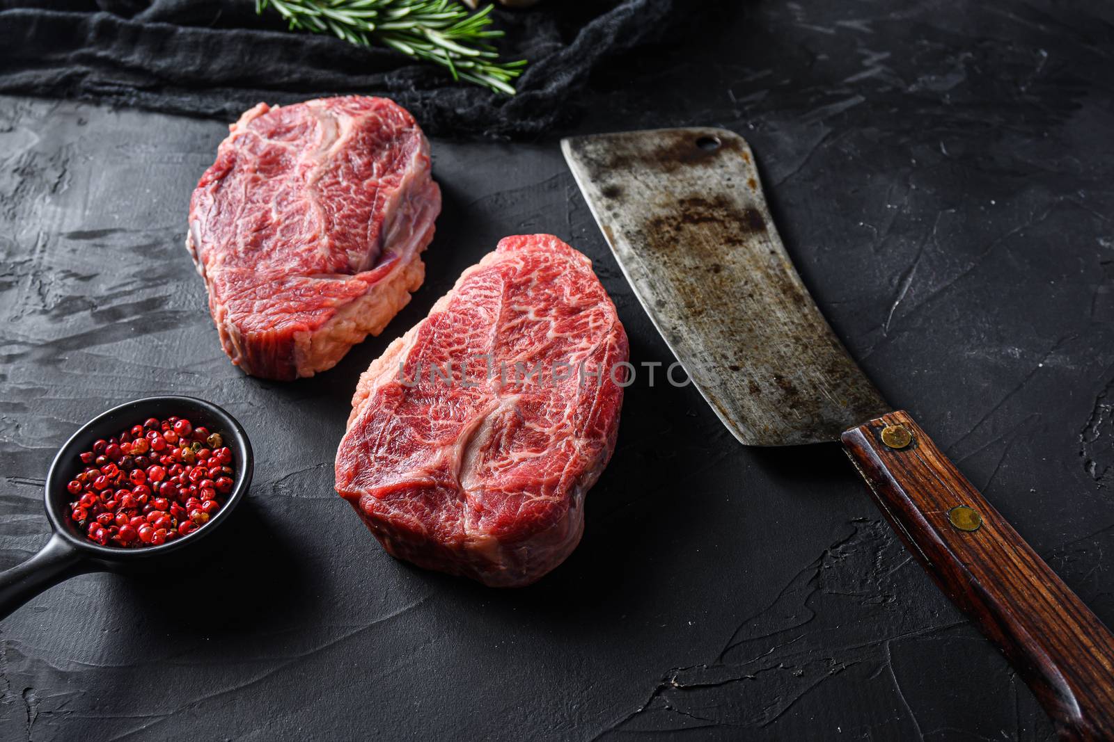 Raw top blade cut organic meat ner butcher meat clever knife for bbq or gtrill top view over black stone background close upside view selective focus.
