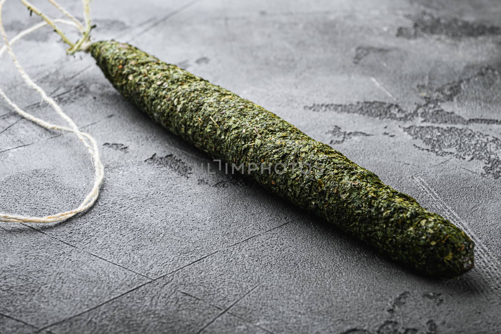 Spanish dry salami sausage fuet in herbs on grey textured background.