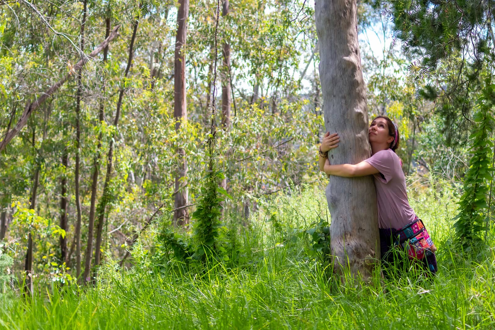 Real woman in hippie attitude hugging a tree in the middle of the forest. face mask