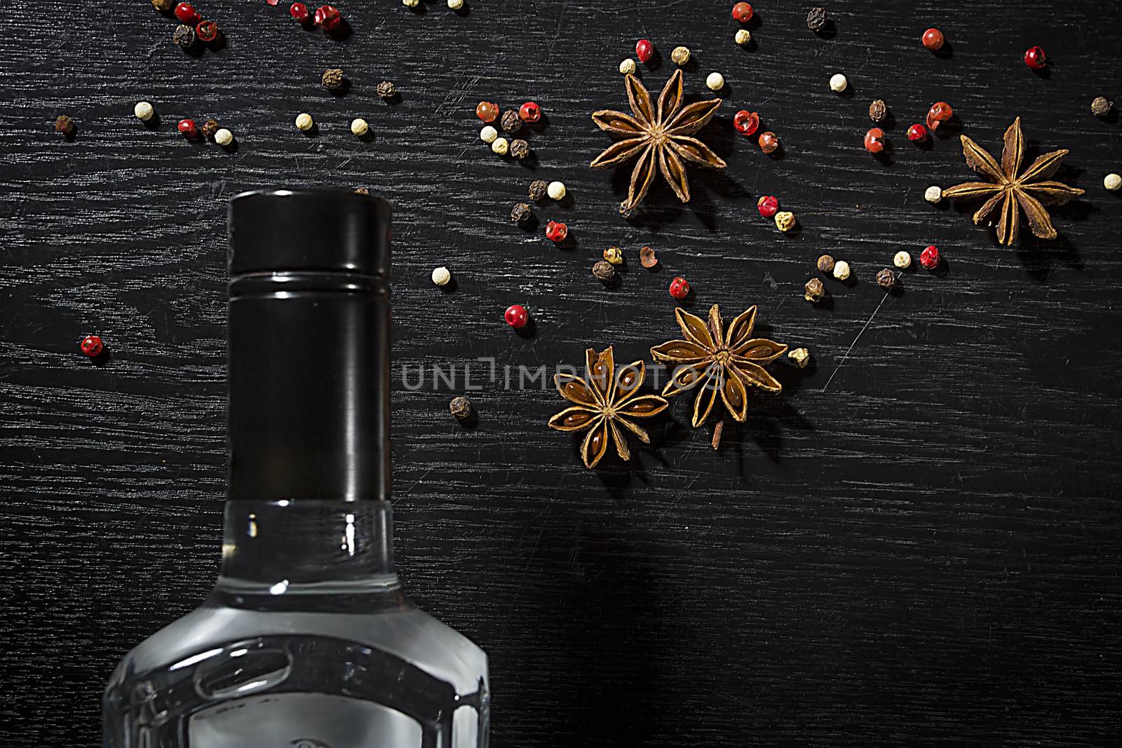 Bottle of anise vodka and spices on wooden black background