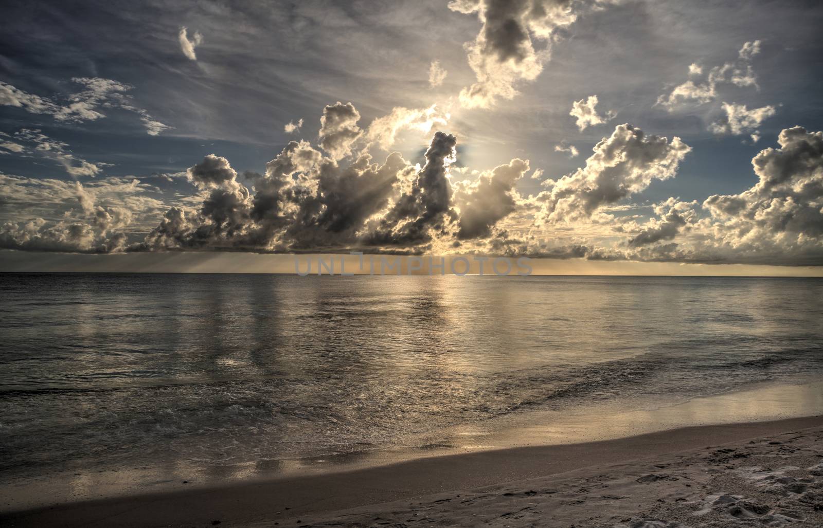 Sun peeks through the clouds over the ocean at sunset by steffstarr