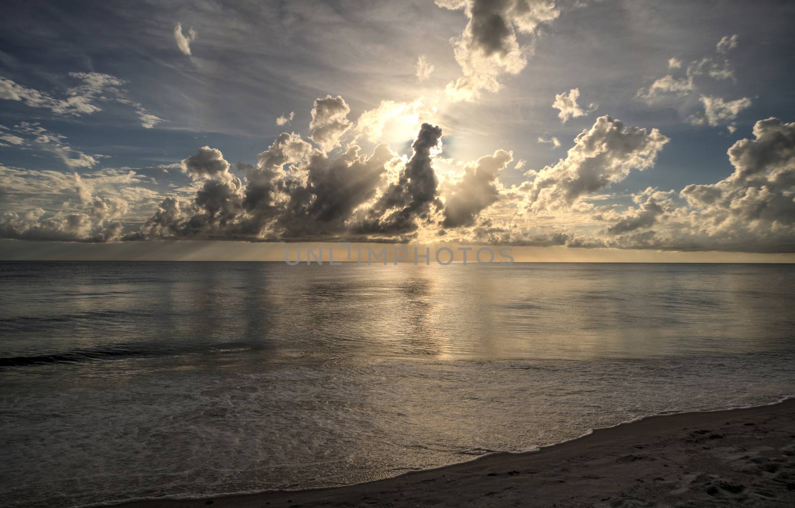 Sun peeks through the clouds over the ocean at sunset in Naples, Florida