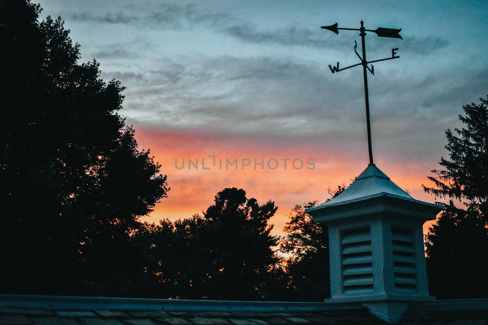 A Blue and Orange Sunset Over a Rooftop With a Weathervane by bju12290