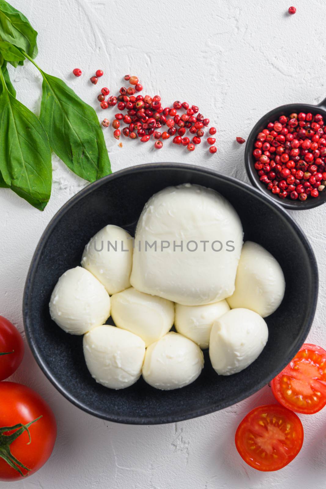 Mozzarella cheese in black bowl, basil tomato cherry balsamic black slate stone copy space. Ingredients for Caprese salad on white background close up vertical.