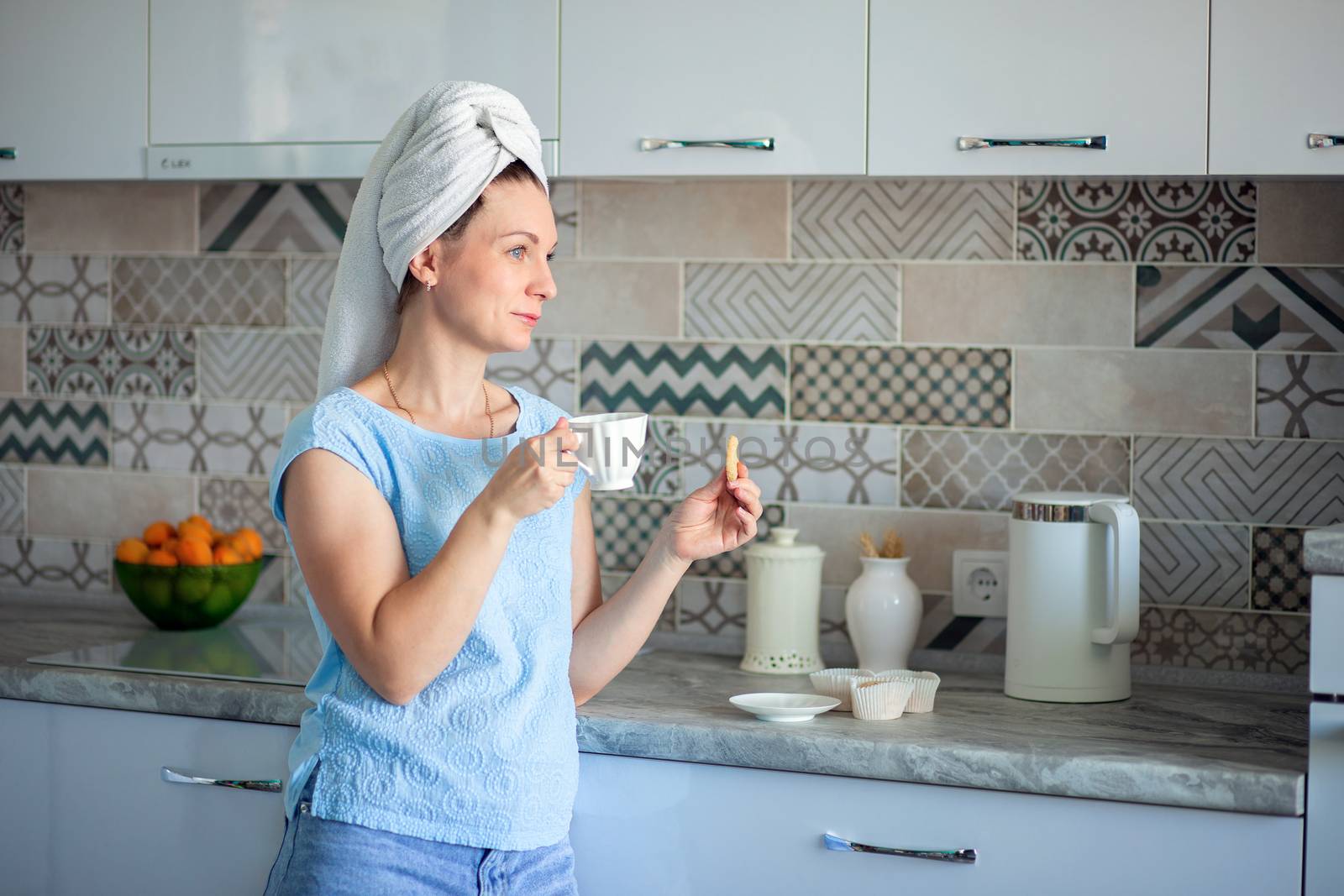 Happy Girl with a towel on her head sutra drinks coffee with cookies for breakfast in his own kitchen at home by borisenkoket