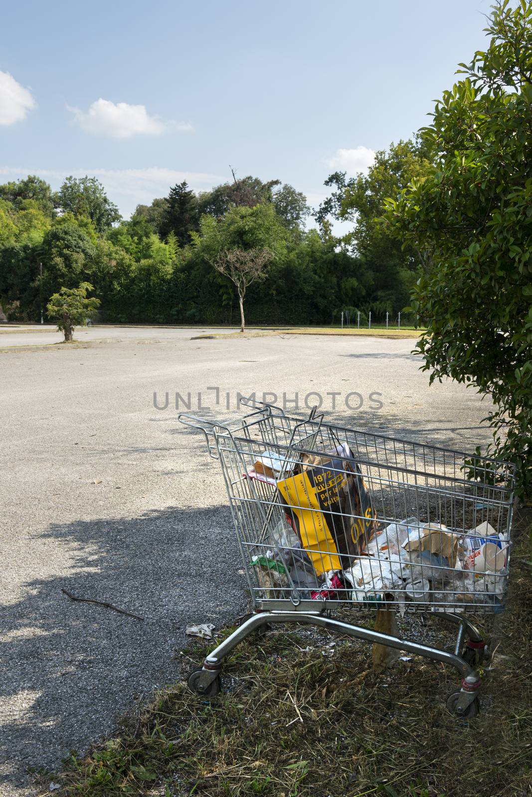 a supermarket trolley with rubbish abandoned in a parking lot