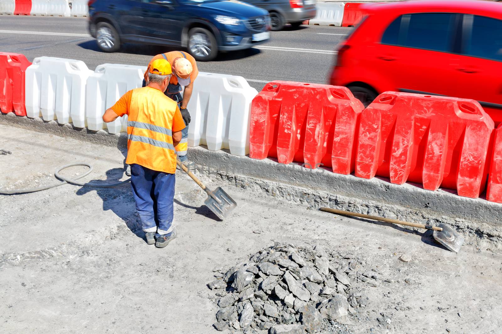 Road workers knock down old concrete during road repairs and shovel a work area. by Sergii