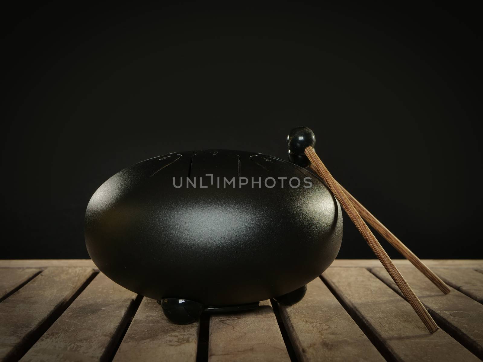Steel tongue drum rare music playing instrument, made from propane tank and also known as tank drum or hank drum similar to Pantam.  On wooden surface and black background