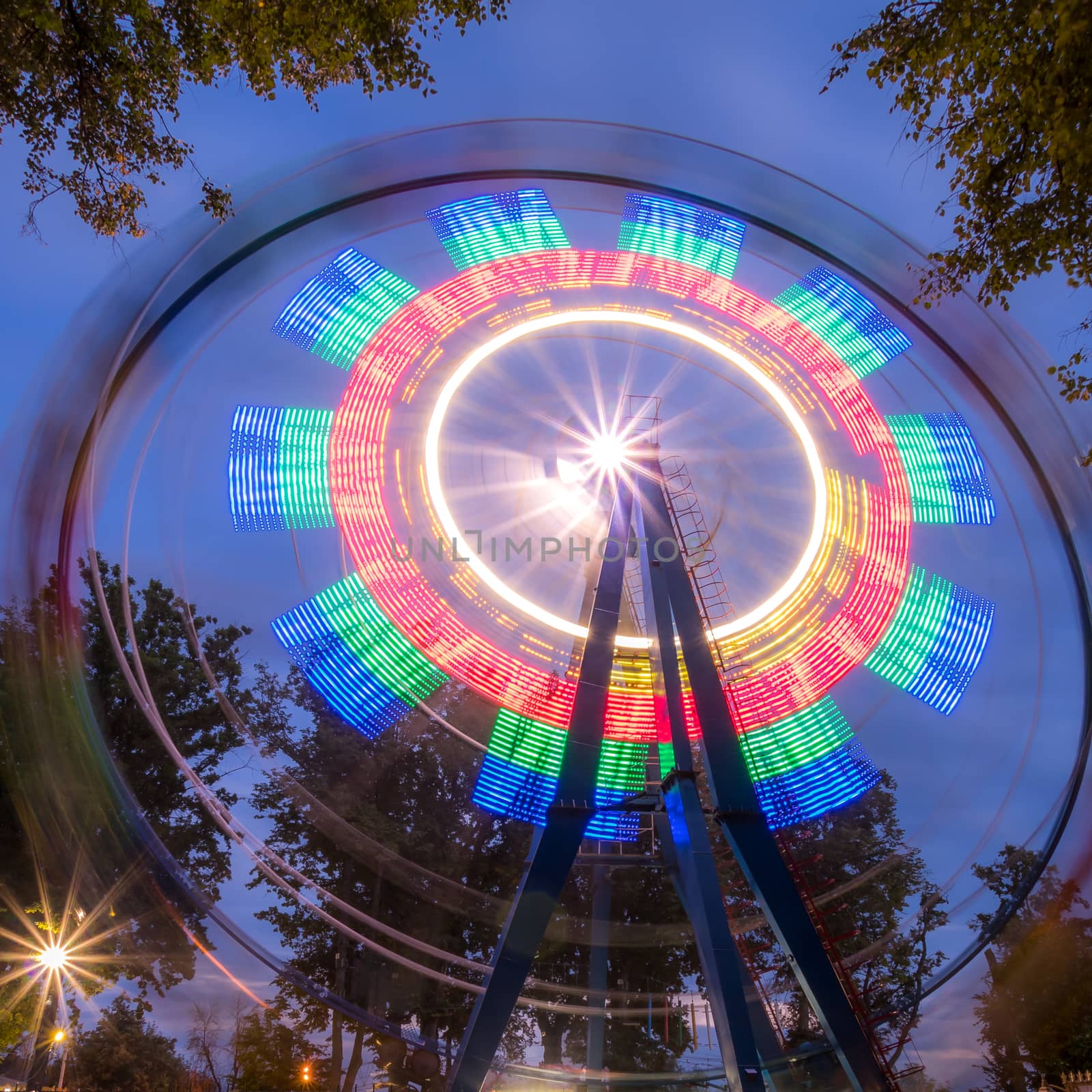 Rotating Ferris wheel in a night park with neon lighting against the sky.