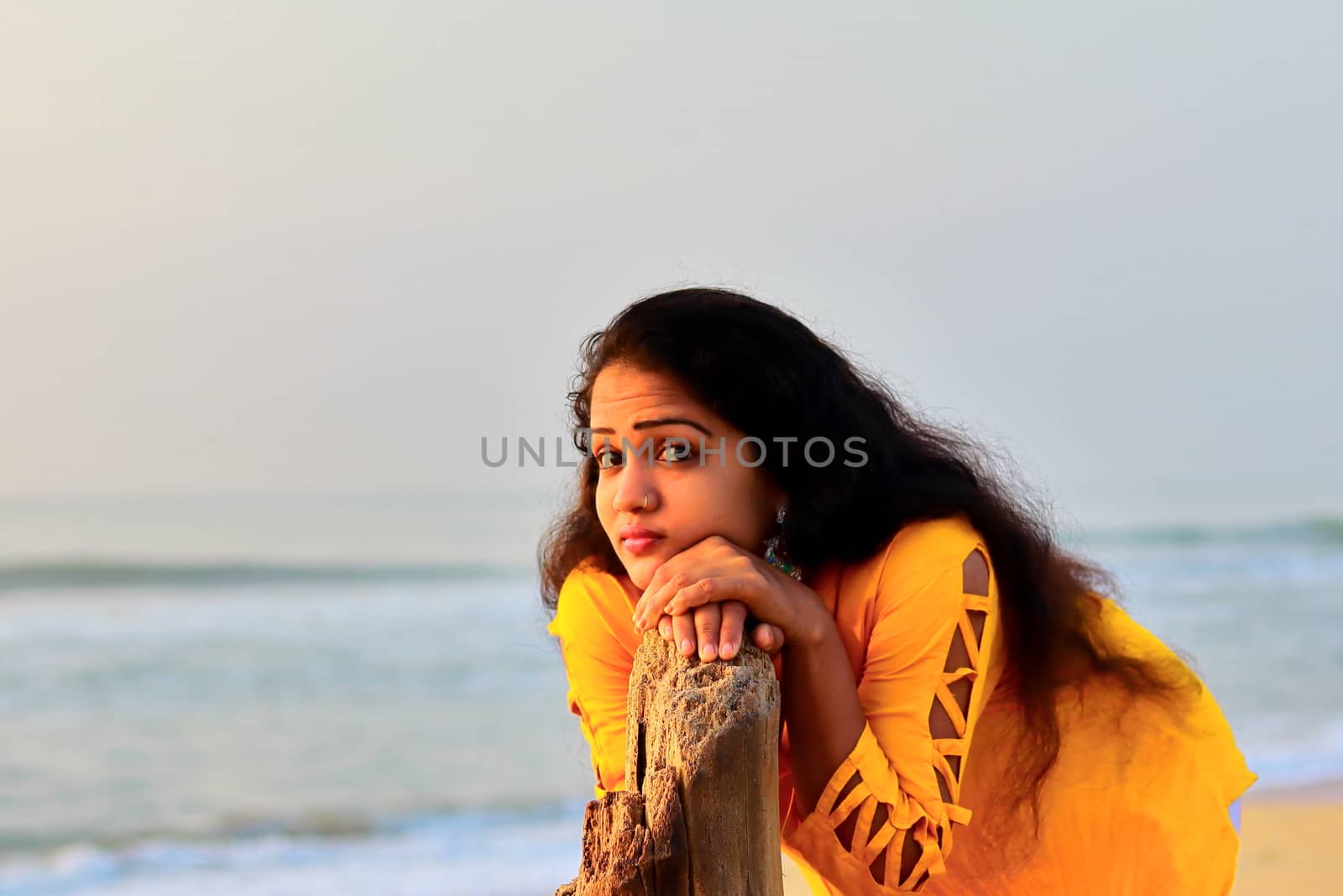 A gorgeous girl standing on the seashore with the help of dry tree wood, outdoors portrait