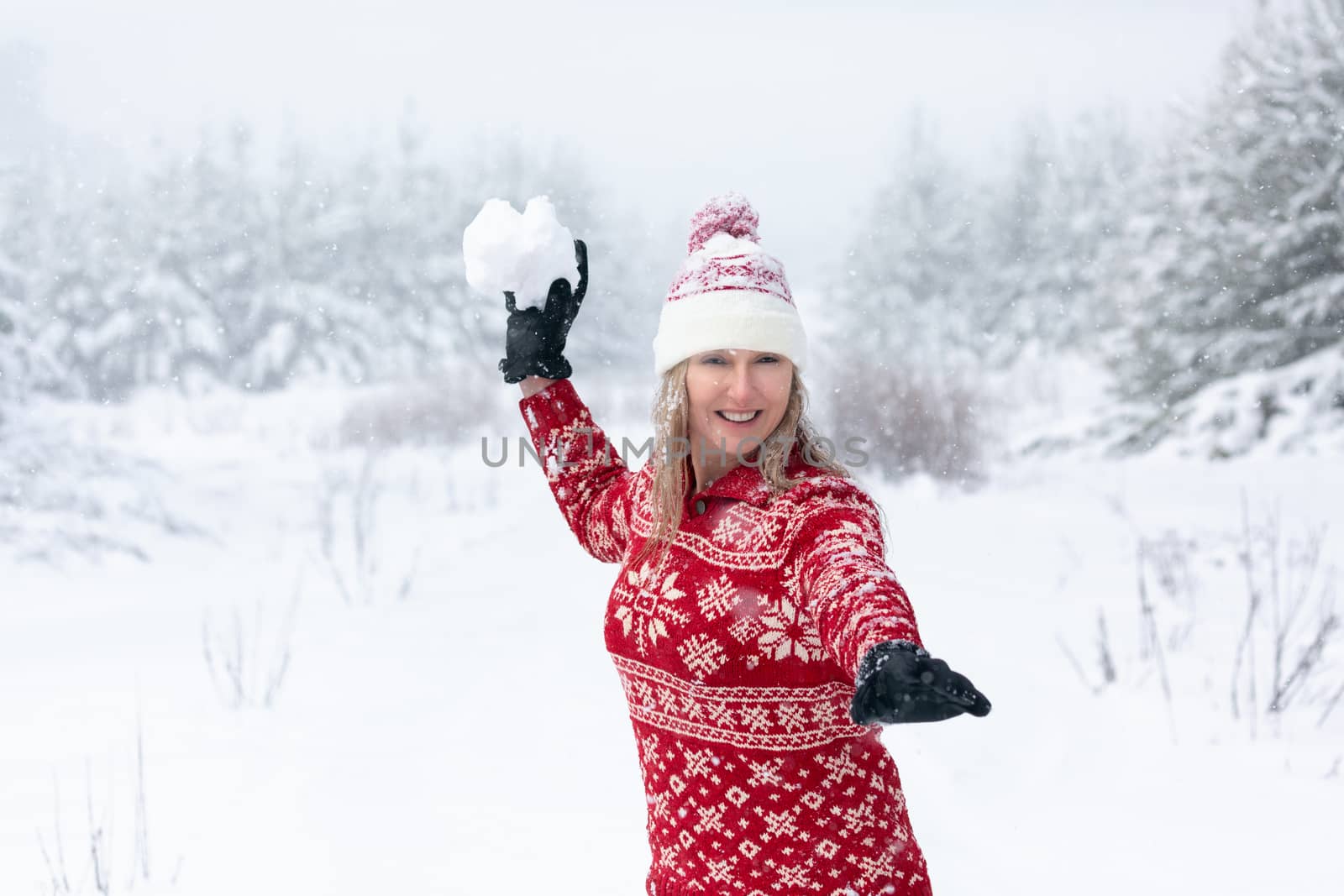 Woman wearing red snowflake sweater and beanie is throwing a huge snowball