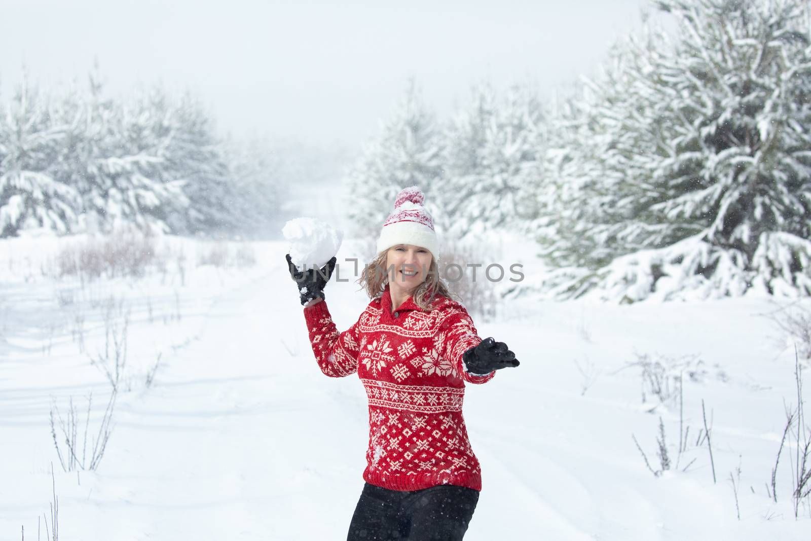 Happy woman throwing a large snowball in winter landscape of pine trees by lovleah