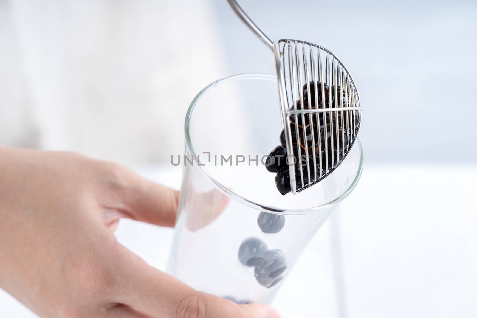 Making bubble tea, scoop and pour cooked brown sugar flavor tapioca pearl bubble balls into cup on white wooden table background, close up, copy space.