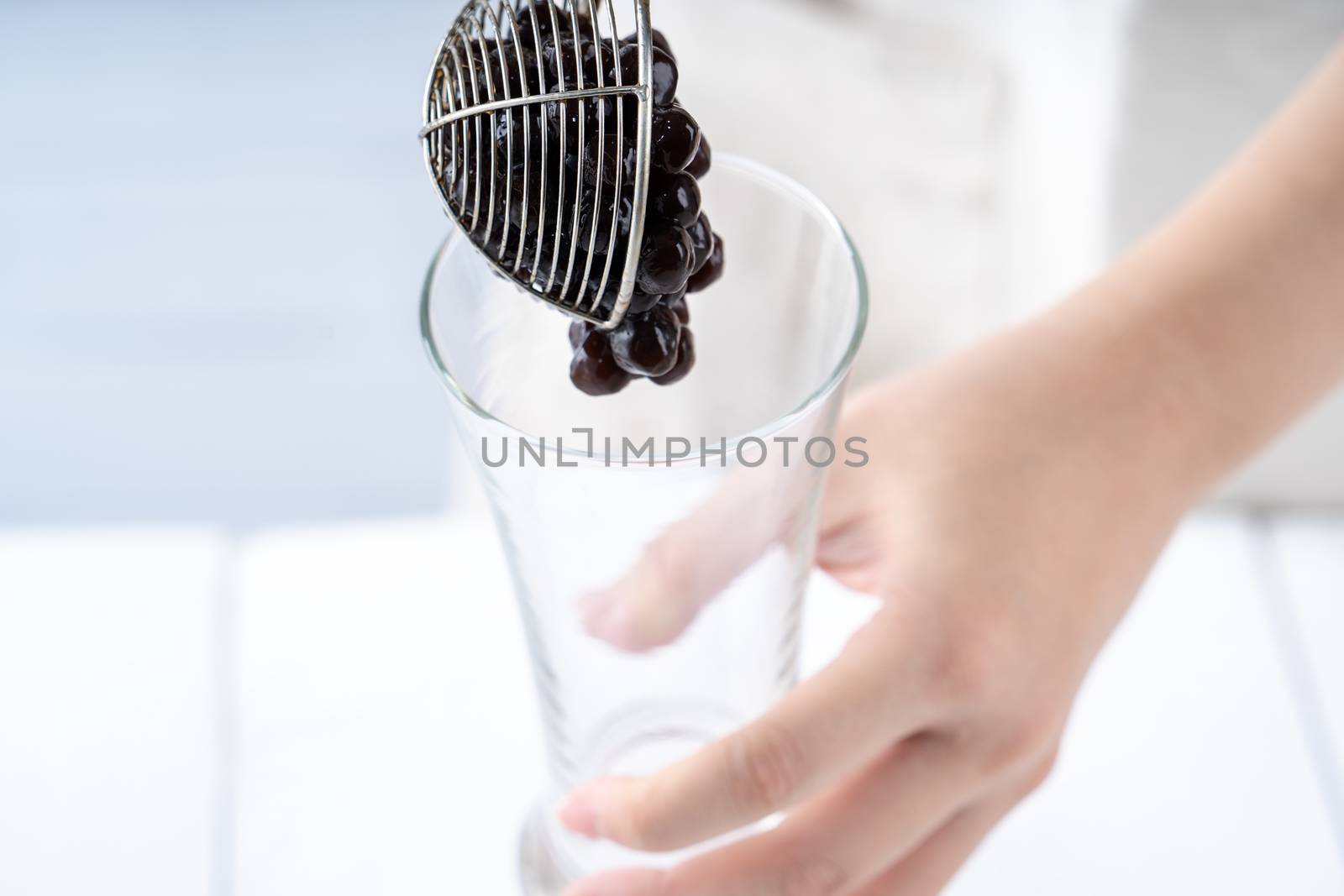 Making bubble tea, scoop and pour cooked brown sugar flavor tapioca pearl bubble balls into cup on white wooden table background, close up, copy space.