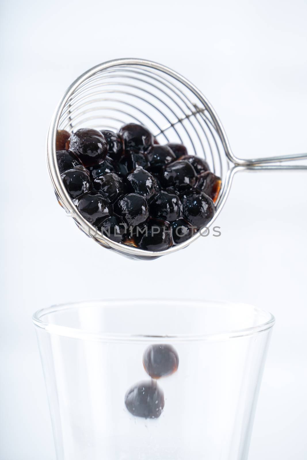 Making bubble tea, scoop and pour cooked brown sugar flavor tapioca pearl bubble balls into cup on white wooden table background, close up, copy space.