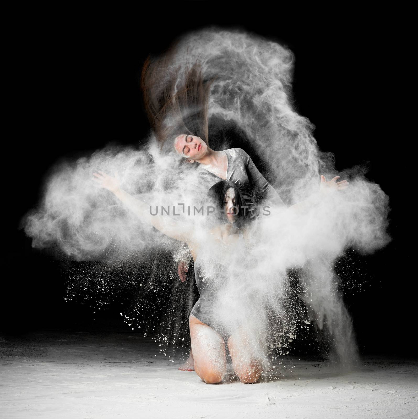 two beautiful young caucasian women in black bodysuits with a sports figure are dancing in a white cloud of flour on a black background, explosion and expresse in motion