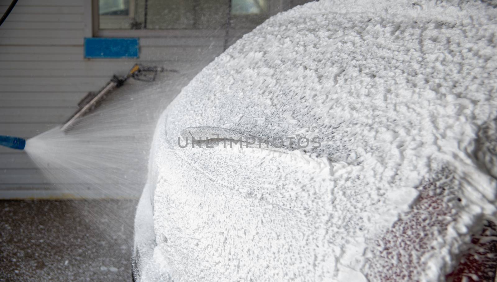 A process of applying soap sud in indoor carwash station - closeup with selective focus and background blur.