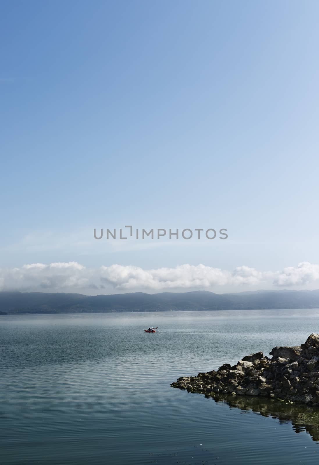 Trasimeno Lake with a sailing canoe , in the foreground seawall in the background lake coast