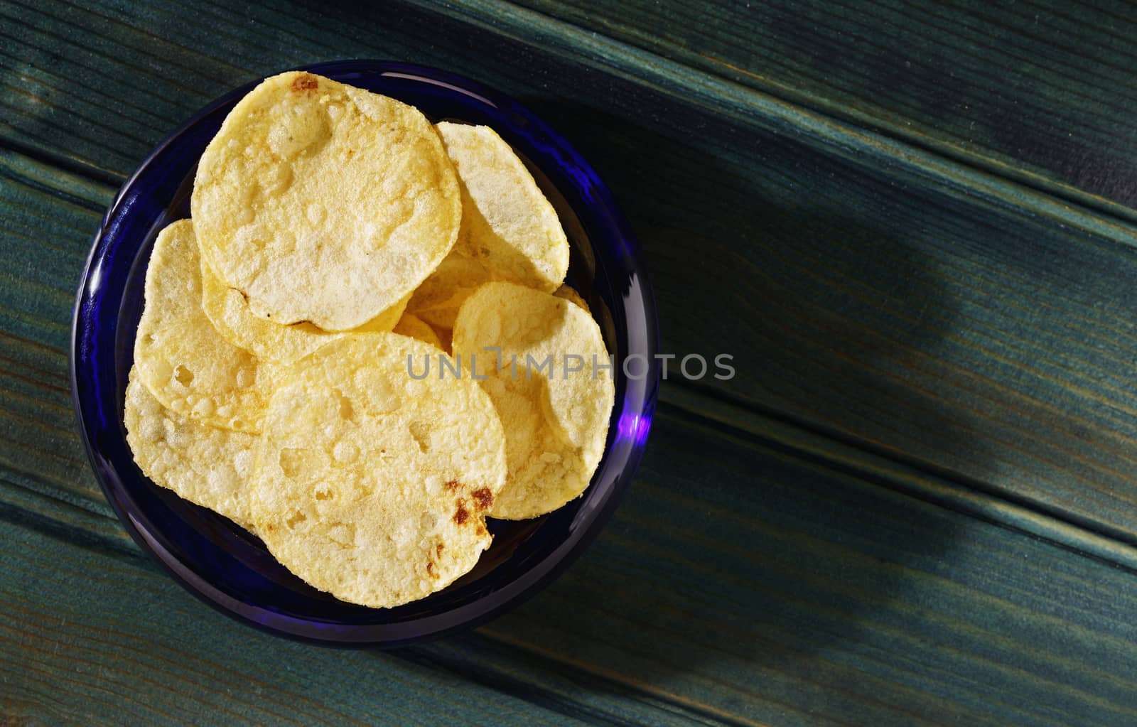 Potato chips or crisps ina blue bowl on dark wooden table,beautiful slices of fried potatoes