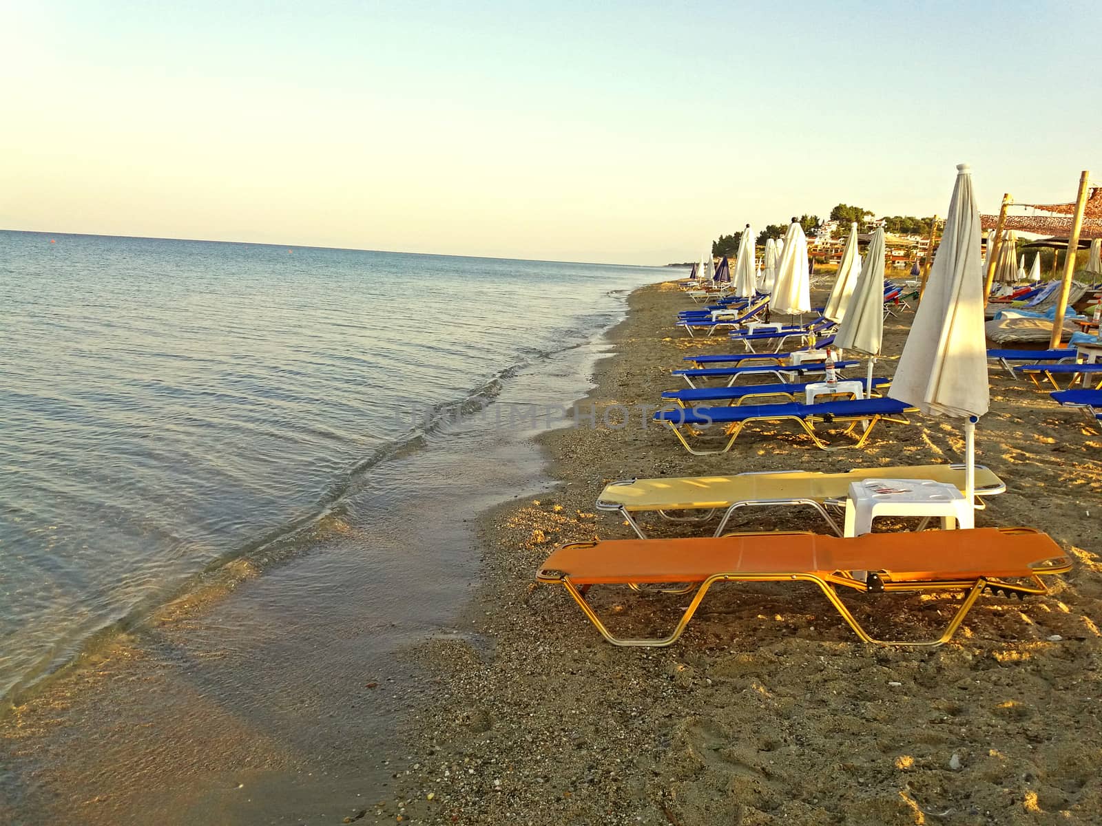 Sunbeds at the shore of the Greek Mediterranean Sea, Greek beach at sunrise by Mindru