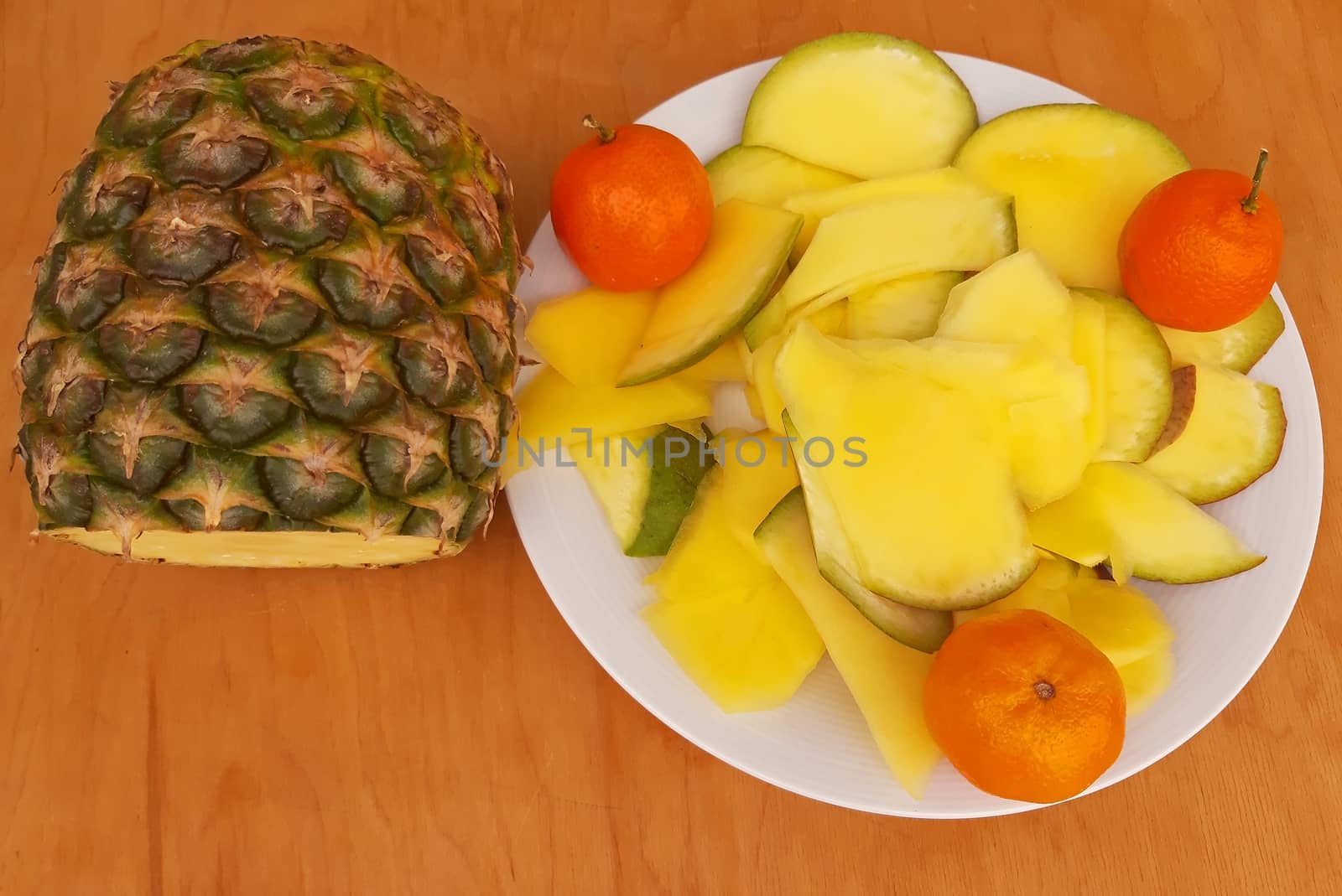 Sliced pineapple and clementines in a plate, wooden background.