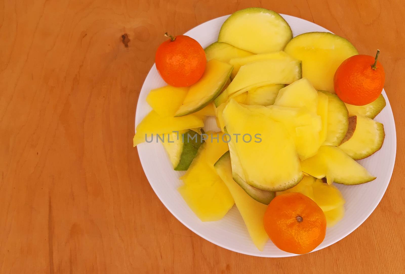 Sliced pineapple and clementines in a plate, wooden background.