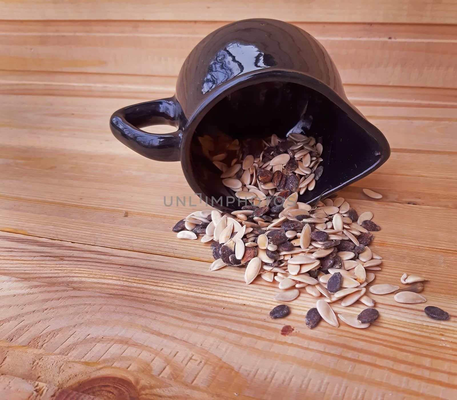 Bowl with seeds overturned on wooden background by Mindru