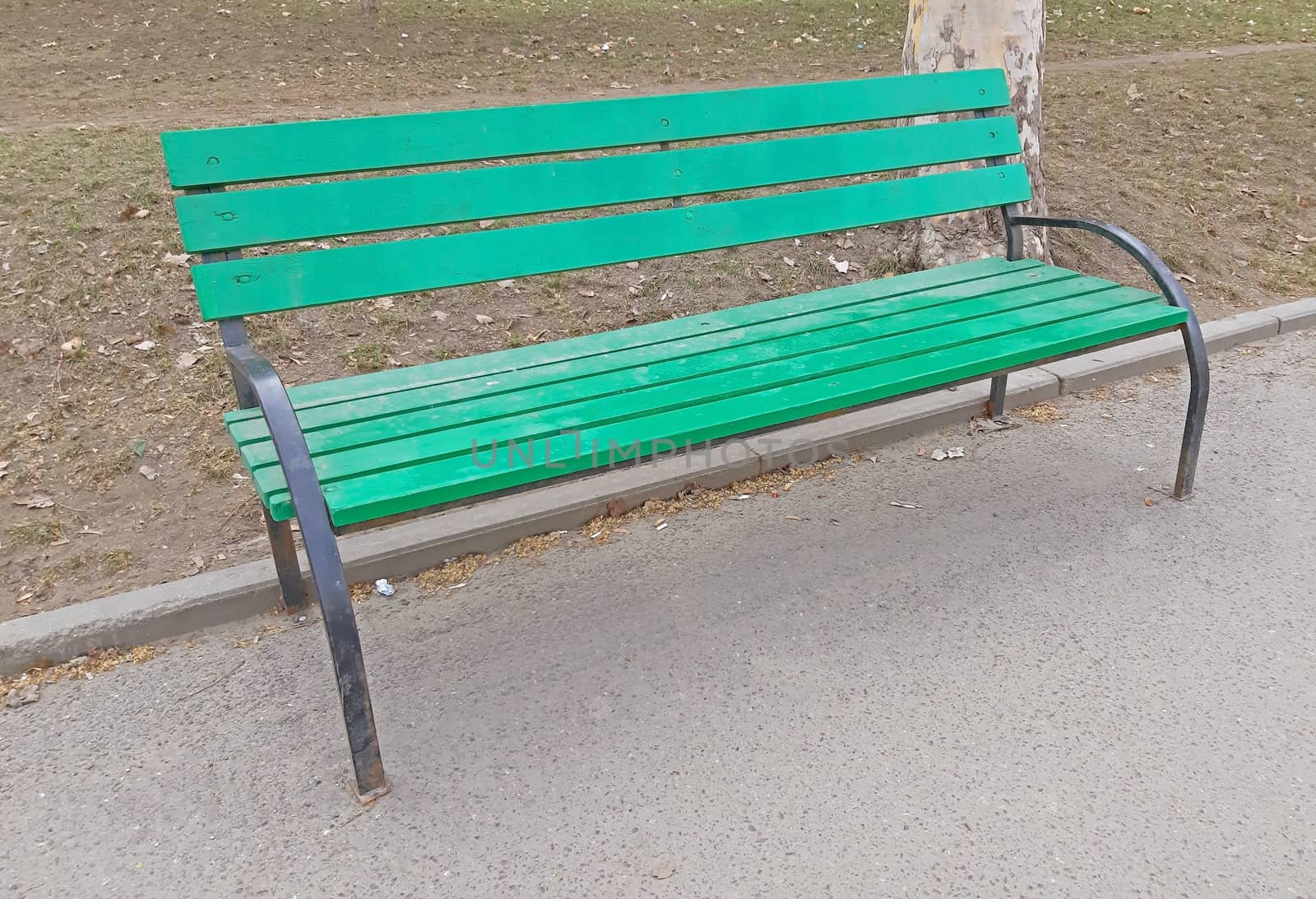 A green chair in the park on the sidewalk.