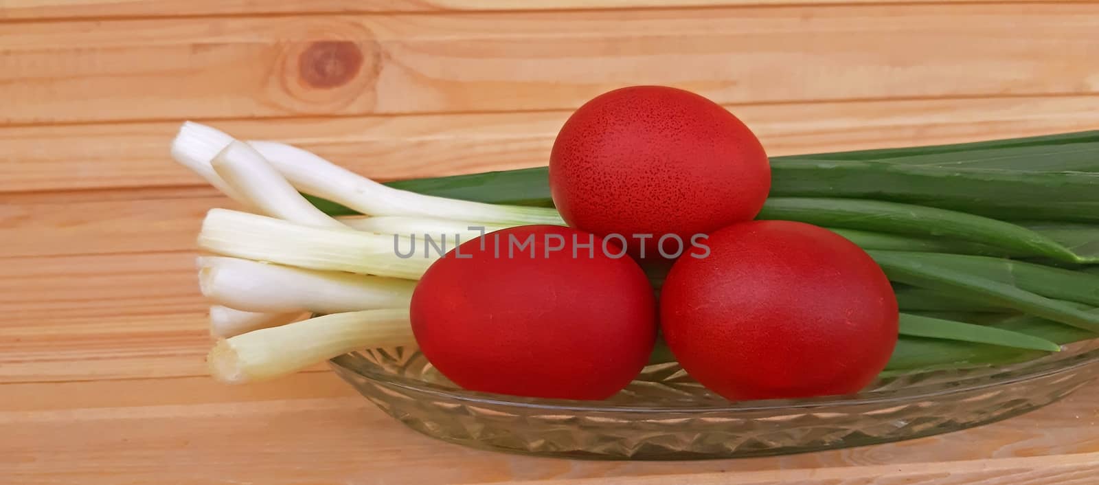 Spring onions and Easter red eggs on wooden background.