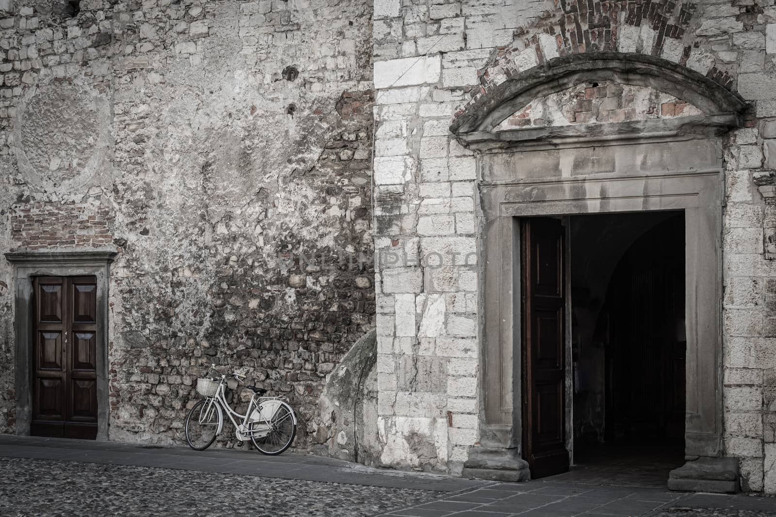 Bicycle leaning against the brick wall of a church with the door by brambillasimone