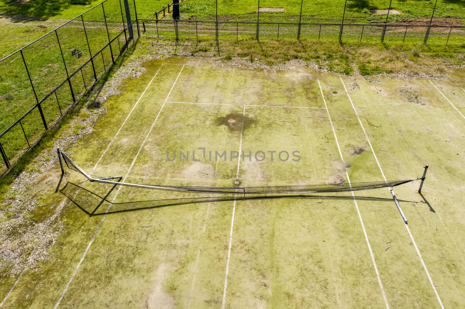 An aerial view of an old unused tennis court in disrepair in a public park in a small regional township