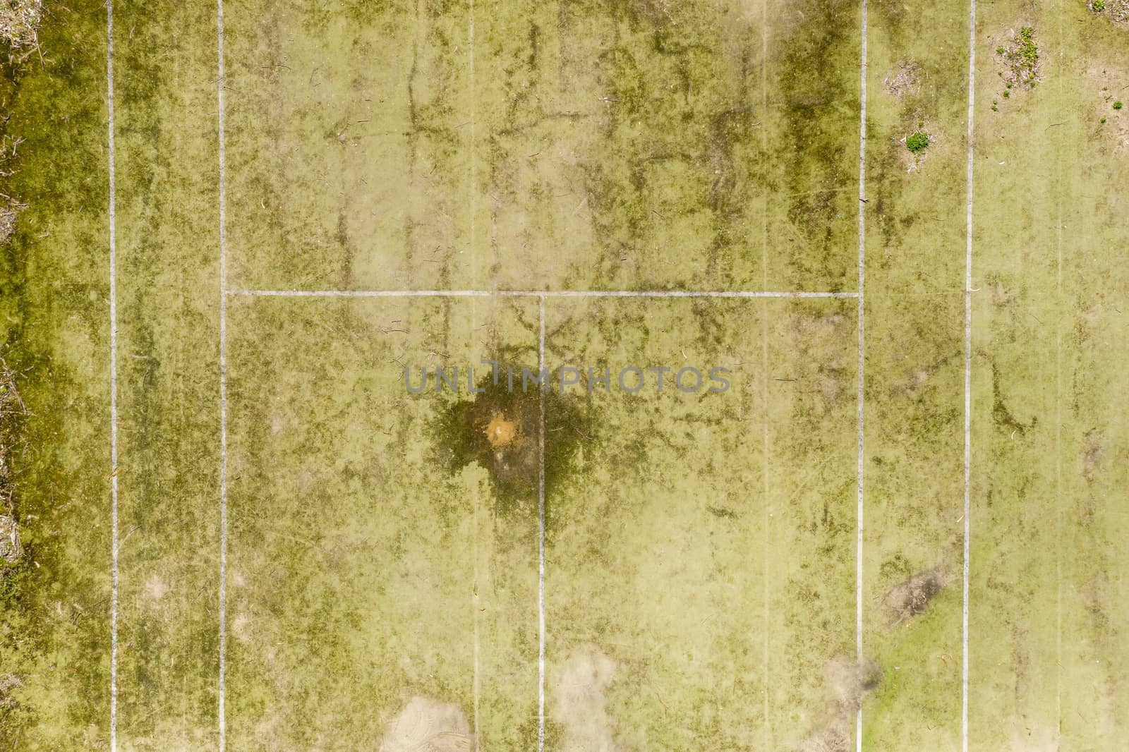 An aerial view of an old unused tennis court in disrepair in a public park in a small regional township