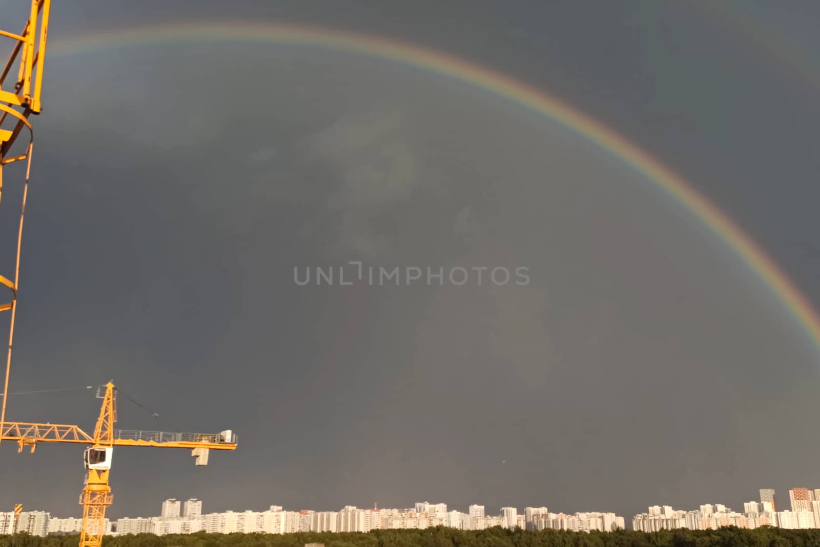 Tower cranes against the sky with clouds and rainbow.