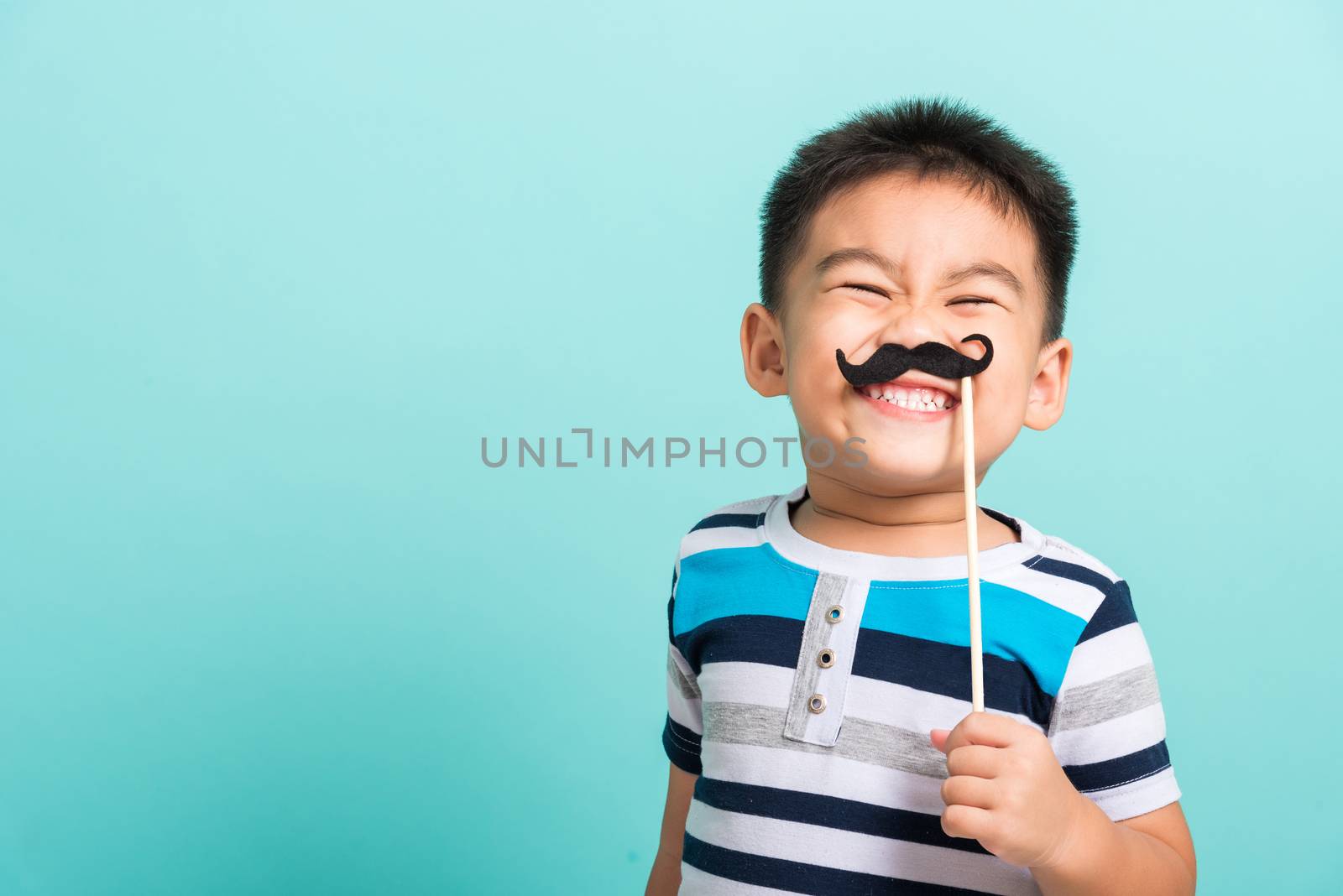 Funny happy hipster kid holding black mustache props for the photo booth close face, studio shot isolated on a blue background, Men health awareness, Prostate Cancer Awareness