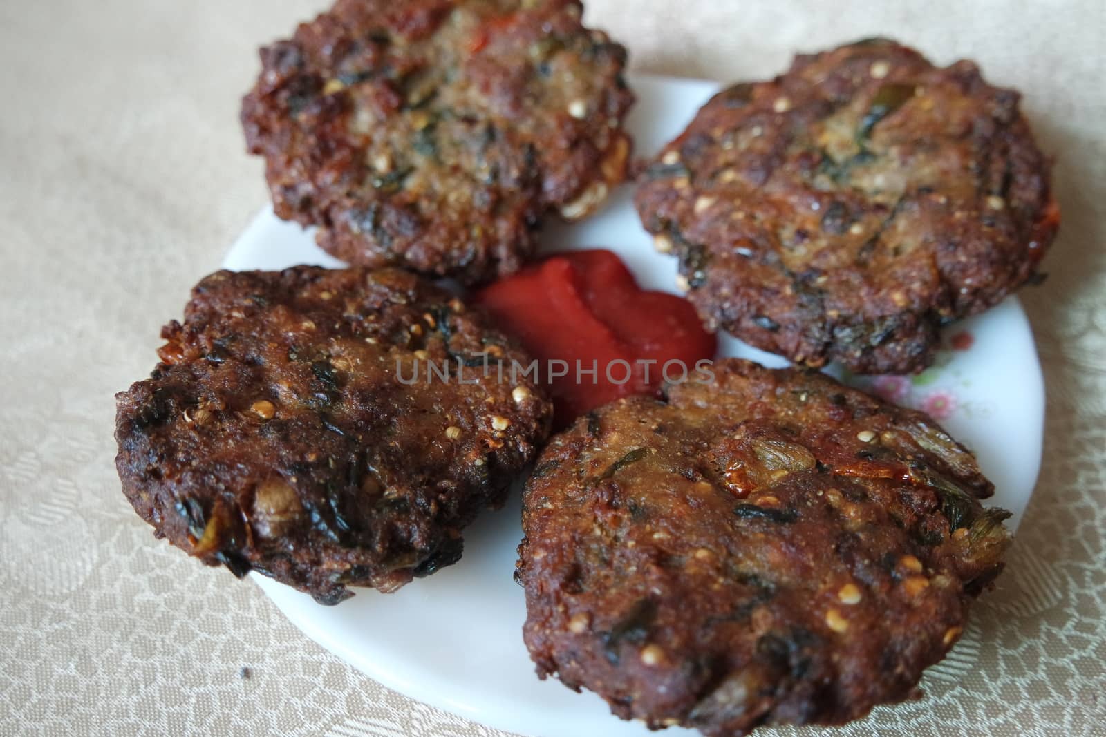 Delicious spicy fried round kebab served in white ceramic plate on a wooden floor with red sauce.