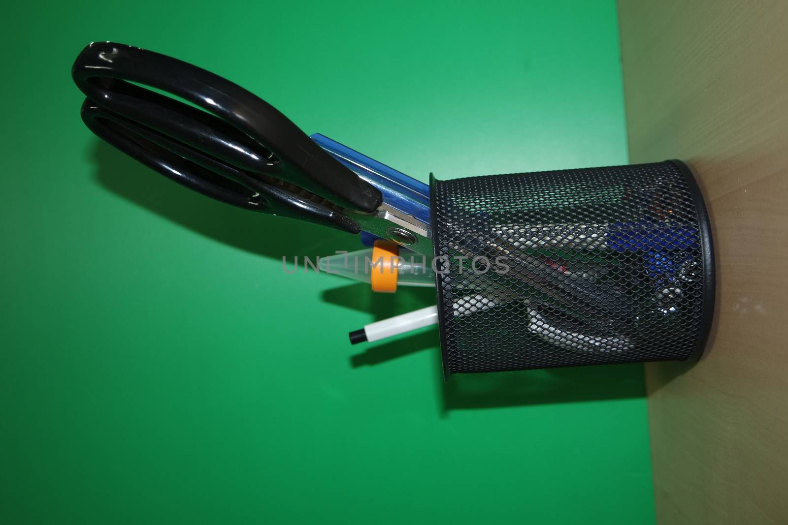 Closeup view of a stationery pot containing stationery items. stationery pot in front of a green background.