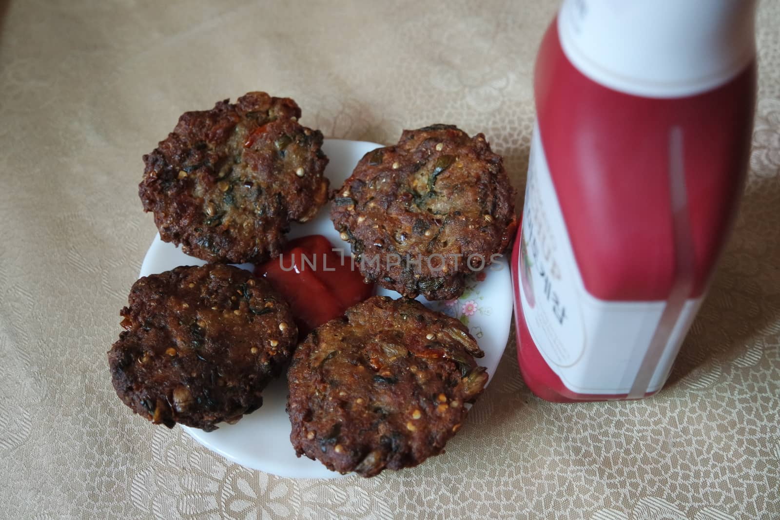 Delicious spicy fried round kebab served in white ceramic plate on a wooden floor with red sauce.