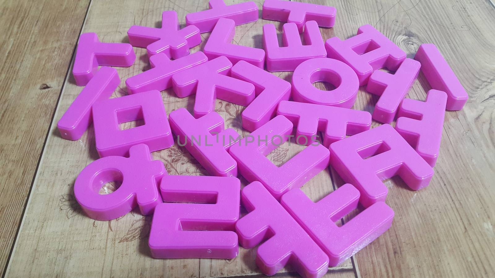 Set of plastic alphabet letters placed on a wooden floor. Alphabet set is used for educating children to learn words and language