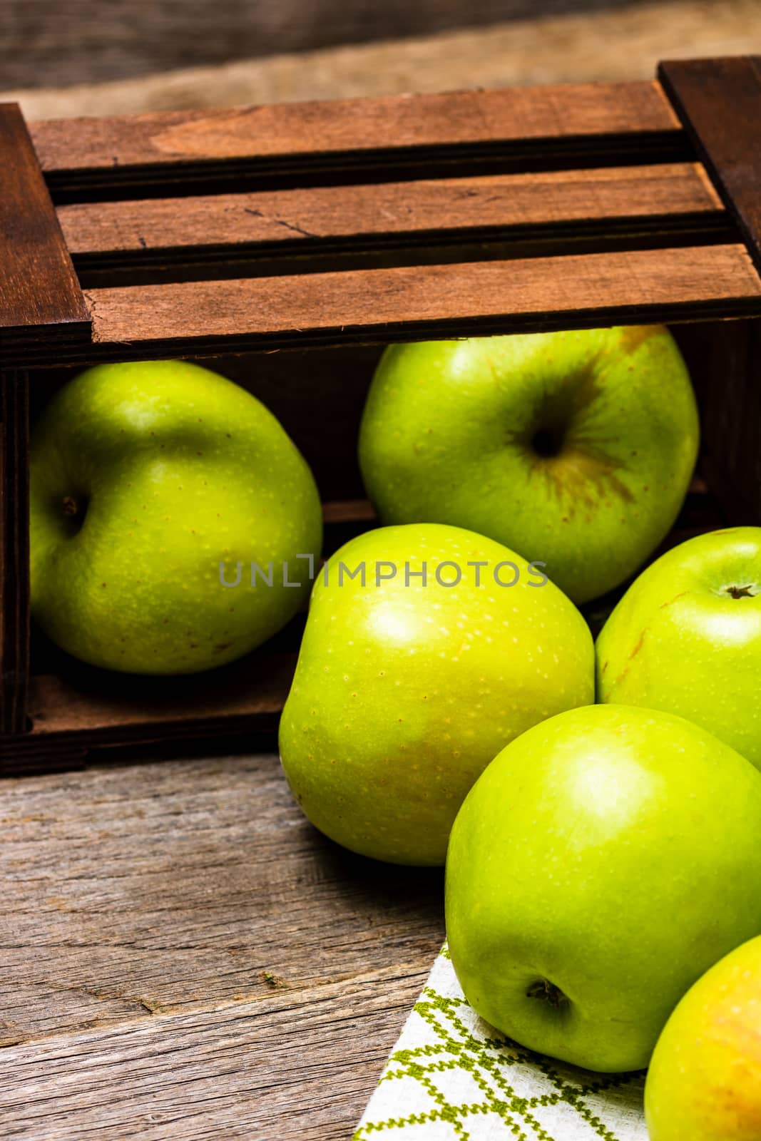 Wooden crate with ripe green apples on wooden table.