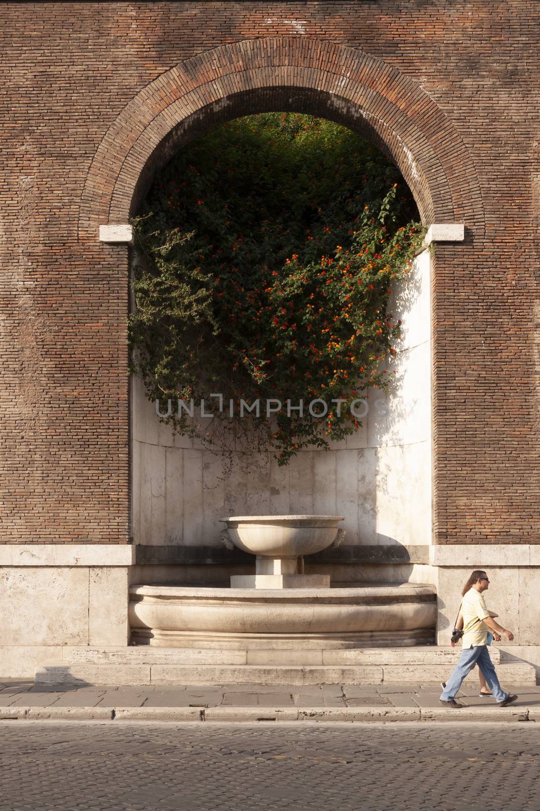 Rome, Italy - June 27, 2010: A tourist couple passes in front of the Fountain of the Imperial Forums, Rome.