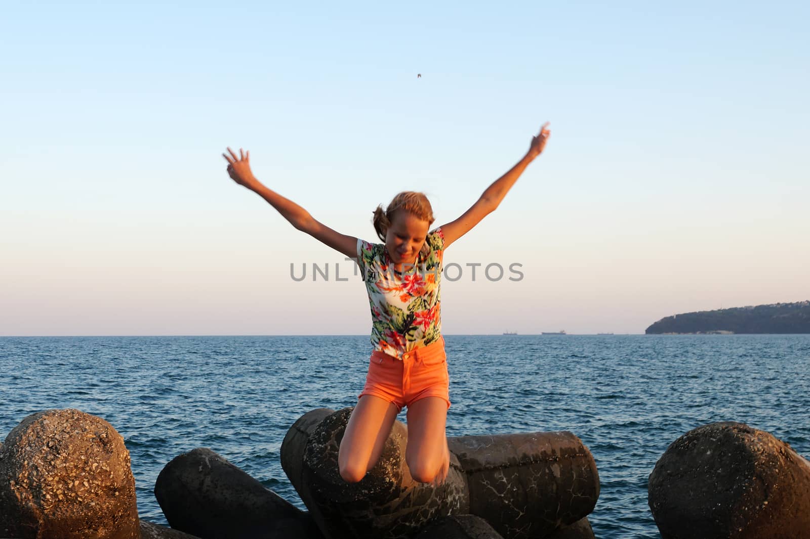 joyful teenage girl with raised arms in a jump against the background of the sea by Annado