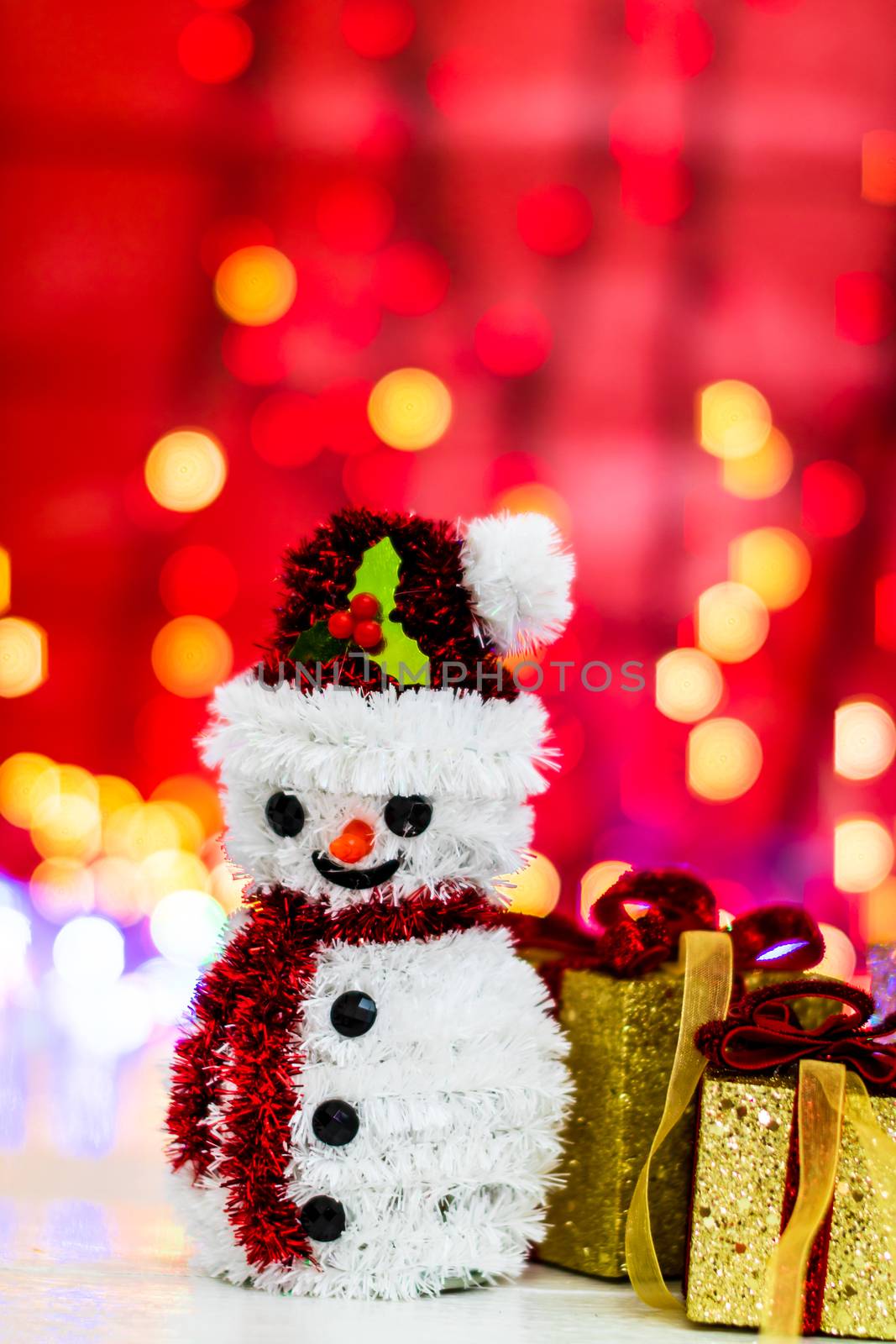 Snowman Christmas figurine near glittery gifts isolated on blurred background of lights. Christmas decorations isolated