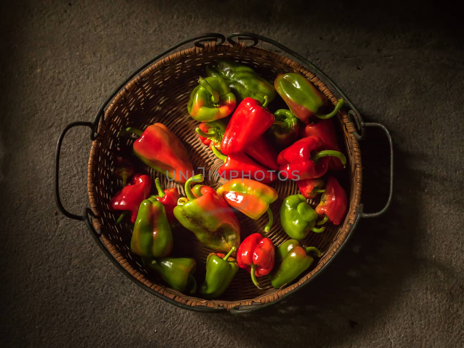 Basket with green and red peppers on a grey stone surface