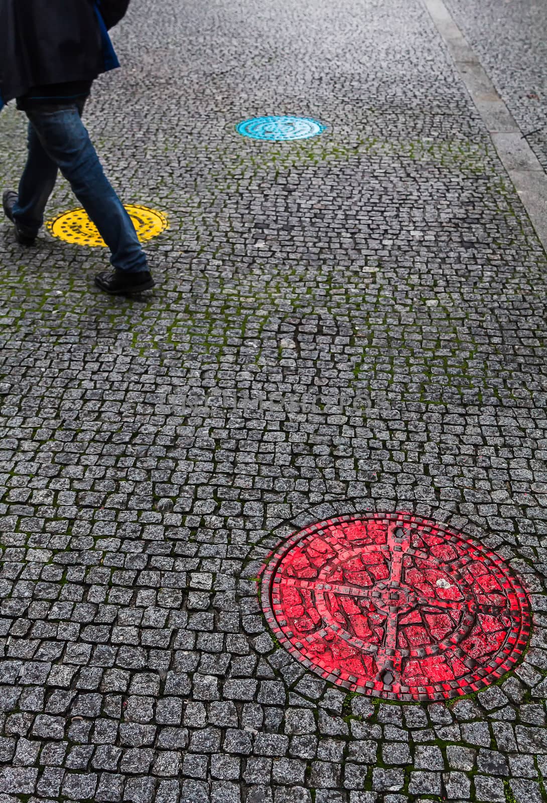 man crossing the pavement with colorful sewer covers. Porto, Portugal.