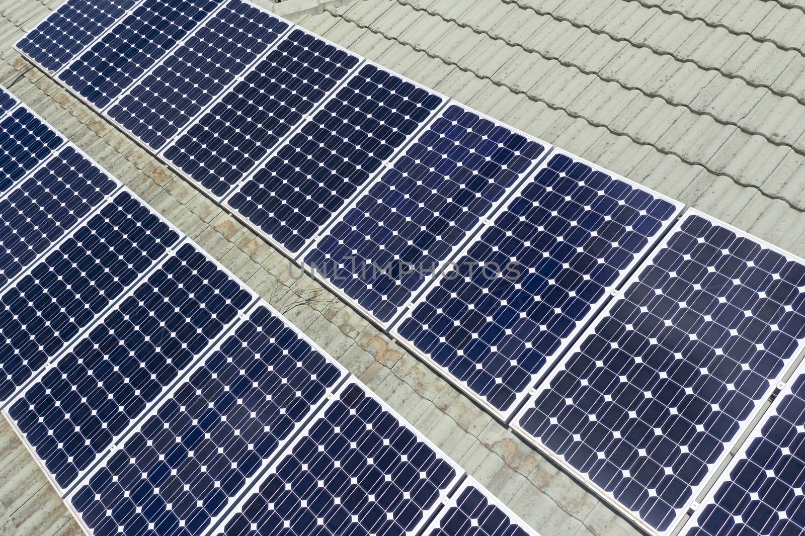 Blue solar panels on a green tiled roof in the bright sunshine.